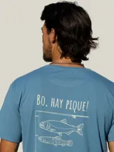 Remera blanca de manga corta con estampa en la espalda en color azul que incluye la frase 'Bo, hay pique!' y dibujos de peces y una caña de pescar.