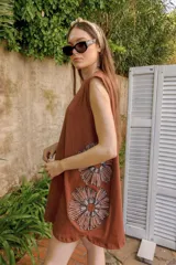 Vestido corto sin mangas, color terracota, con corte holgado y bordados grandes de flores estilizadas en blanco y negro en la parte inferior delantera.