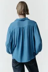 Camisa de manga larga con cuello solapa, confeccionada en tejido fluido. Presenta detalle de jaretas verticales en el frente y cierre frontal con botones forrados al tono.