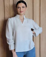 Blusa de algodón con diseño a rayas verticales finas, cuello mao con volados y escote en V. Presenta mangas largas abullonadas con puños elásticos terminados en volados.