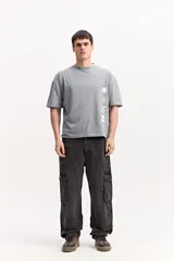 Remera boxy de manga corta color gris con efecto acid wash y estampas geométricas blancas dispuestas verticalmente en el frente. Tiene corte amplio y diseño de estilo urbano.