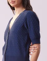 Cárdigan blanco tejido con escote en V, abertura frontal con botones y mangas cortas abullonadas con puño.