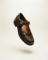 Mocasín de cuero color bordó con textura trenzada en la puntera. Presenta una solapa desmontable con flecos y detalle de perforaciones, junto con una hebilla lateral metálica. Diseño versátil que permite transformar el calzado.