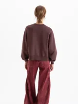 Buzo de corte oversize color marrón chocolate, con cuello redondo y diseño estampado de flores en la parte frontal. Presenta mangas largas con puños ajustados.