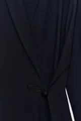 Blazer de corte fluido confeccionada en mezcla de viscosa, con cuello solapa, manga larga con puños abotonados y cierre frontal cruzado con botón único.