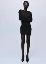 Vestido corto entallado de color negro, con cuello redondo y manga larga. Presenta un diseño de espalda abierta con tiras y un delicado detalle de encaje en el bajo. Incluye forro interior y cierre de cremallera en la parte posterior.