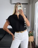 Blusa negra de tela Cey, con cuello mao y escote en V con cierre. Mangas cortas con detalle de encaje marrón en los hombros.