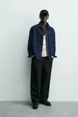 Chaqueta de denim de algodón en color azul oscuro con corte relaxed fit. Presenta cuello de solapa, cierre frontal con botones metálicos y tres bolsillos de parche en el delantero. Las mangas son largas con puños abotonados.