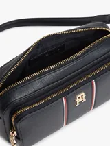 Cartera bandolera Tommy Hilfiger de color azul marino, con acabado granulado, cierre de cremallera superior, compartimento principal y bolsillo exterior con cremallera. Incluye correa extraíble para el hombro, detalles distintivos con franjas verticales y la insignia del monograma TH en metal dorado en la parte delantera.