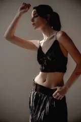 Top corto de encaje negro con breteles finos y detalle de plumas desmontables en el escote. Presenta un diseño ajustado al cuerpo con forro interior.