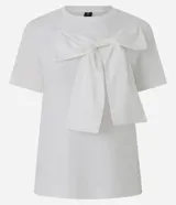 Remera de manga corta confeccionada en algodón, con cuello redondo y diseño recto. Presenta un lazo grande aplicado en la parte frontal que aporta volumen a la prenda.