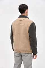 Campera de estilo outdoor con diseño de bloques de color, confeccionada en una combinación de sherpa y paneles de nylon capitoneado. Presenta cierre frontal con botones a presión, cuello alto, bolsillos laterales y un bolsillo en el pecho con cierre. Incluye puños elásticos y detalles bordados en la manga.