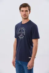 Remera azul marino de manga corta con cuello redondo, confeccionada en mezcla de algodón y poliéster. Presenta un estampado frontal circular de inspiración vintage con diseño de velero y tipografía alusiva a clubes deportivos.
