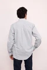 Camisa de corte clásico confeccionada en algodón, con diseño de rayas verticales en tonos claros, cuello abotonado y manga larga. Presenta un pequeño bordado en el pecho.