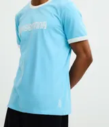 Remera de algodón color celeste con cuello redondo y bordes de mangas en color blanco. Presenta la palabra 'ARGENTINA' estampada en el pecho con tipografía blanca.