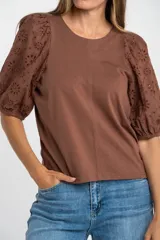 Remera de algodón color rosado con mangas cortas abullonadas de broderie con diseño floral calado. Presenta cuello redondo y costura vertical central en el frente.