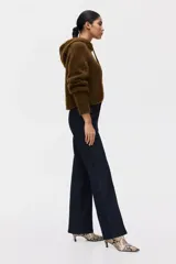 Jean de tiro alto con corte acampanado desde la rodilla. Presenta un diseño de denim oscuro con pliegues frontales y traseros, cierre con botón oculto y bolsillos traseros decorativos.