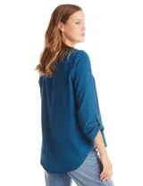 Blusa de color blanco con escote en V y cuello mao. Presenta mangas largas con presilla y botón para regular el largo, y un corte holgado con ruedo redondeado.