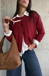 Cardigan de punto con textura trenzada en color bordó, con cuello redondo y cierre frontal mediante botones tipo alamar. Presenta mangas largas con puños acanalados y un corte clásico.