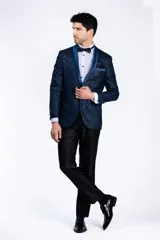 Ambo de ceremonia tipo smoking, compuesto por un saco azul con diseño jacquard y solapa chal de raso al tono, y un pantalón negro satinado de corte slim fit.