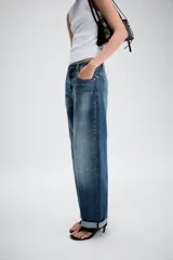 Jeans de tiro medio con diseño de cinco bolsillos, pernera holgada y bajo con vuelta. Cierre frontal con cremallera y botón.