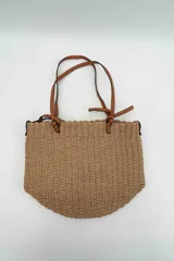 Bolso de mano tipo tote confeccionado en tejido texturizado efecto rafia en color beige, con asas dobles finas de cuero sintético marrón y detalles de nudos en los extremos.