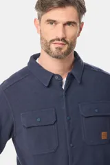 Camisa azul marino de poliéster con textura polar, corte recto, cuello camisero, cierre frontal con botones a presión, dos bolsillos de parche con solapa abotonada en el pecho y puños abotonados.