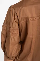 Blusa de algodón color marrón con cuello en V, mangas tres cuartos con puños elásticos y detalles de encaje y alforzas en el frente.