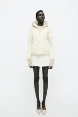 Cazadora de mujer con diseño híbrido, presenta un panel frontal acolchado con costuras en chevron y mangas y laterales en tejido liso. Cuenta con cuello alto, capucha ajustable con cordones elásticos y cierre frontal mediante cremallera.