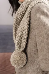 Bufanda tejida a mano en punto arroz color crudo, con detalle de pompón en uno de los extremos.