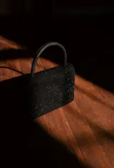 Cartera de mano negra con brillo, de forma rectangular y asa superior.