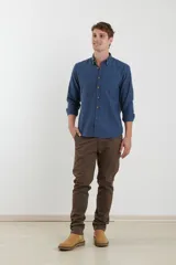 Camisa de vestir blanca de manga larga, con cuello abotonado, bolsillo frontal y botones en tono madera.