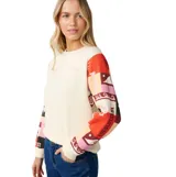 Buzo Rip Curl de color blanco con mangas largas estampadas con diseños coloridos y geométricos, cuello redondo y calce relajado.