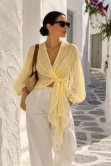 Camisa cruzada de gasa color amarillo claro con diseño de rayas sutiles, escote en V pronunciado, mangas largas abullonadas y lazo ajustable para atar en el frente.