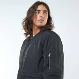 Campera estilo aviador negra, con cierre frontal, cuello redondo y puños y cintura elásticos. Presenta bolsillos de fuelle con doble entrada en la parte inferior y un bolsillo con cierre en la manga izquierda.