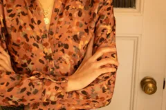 Camisa de crepe estampada con motivos abstractos en tonos marrones, rosados y negros, con cuello clásico y cierre frontal con botones.