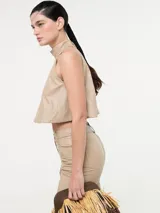 Top corto color beige, estilo halter con cuello alto y espalda descubierta. Confeccionado en eco cuero.
