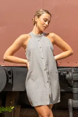 Vestido corto de color beige con cuello halter, diseño sin mangas y cierre frontal con botones dorados.