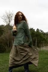 Buzo reversible de tejido fino con sutil lurex, color verde, que puede usarse también como saco. Presenta diseño acanalado con costuras horizontales decorativas en tono contrastante, mangas largas y cierre frontal con botones en forma de flor.