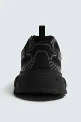 Zapatilla deportiva tipo running con diseño técnico, confeccionada en una combinación de malla y piezas sintéticas. Presenta cordonera curvada y una suela robusta con volumen y diseño irregular.