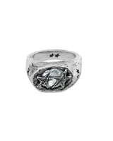 Anillo sello de metal plateado con acabado envejecido y textura rugosa. La parte superior presenta una piedra central de color celeste claro facetada, rodeada por dos estrellas superpuestas con textura. El cuerpo del anillo tiene grabados de estrellas pequeñas.