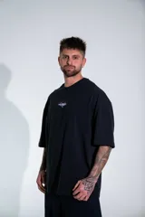 Remera oversize de algodón elastizado en color negro, con diseño gráfico estampado en la espalda que representa un arco gótico con detalles en rojo y texto.