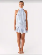 Vestido corto celeste con escote halter, espalda descubierta, falda con volados y pliegues en la cintura.