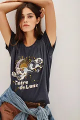 Remera de algodón color gris oscuro con cuello redondo y mangas cortas. Presenta un estampado frontal con motivos celestiales de sol, luna y nubes, con detalles de lentejuelas y la inscripción 'Claire de Lune'.