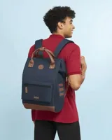 Mochila urbana Cabaia modelo Adventurer Chicago, color azul marino con detalles en cuero sintético marrón. Cuenta con un compartimento principal con cierre, un bolsillo frontal con cierre, asas superiores y base reforzada.