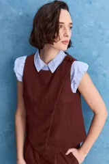Top blanco sin mangas, con cuello redondo, diseño cruzado en el frente y cierre con botones en el hombro.