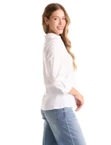 Camisa blanca de algodón con cuello camisero y escote en V. Presenta detalles plisados en el frente, cierre central con botones y mangas tres cuartos con puños abotonados. Los laterales están confeccionados en tejido modal para mayor comodidad.