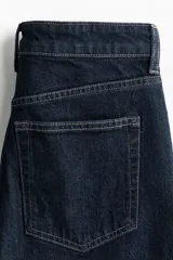 Jean de tiro alto con corte wide leg, confeccionado en denim de algodón con leve stretch. Presenta diseño clásico de cinco bolsillos, cierre frontal con botón y costuras en contraste.