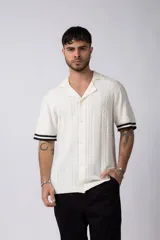 Camisa de punto de manga corta con cuello tipo bowling y cierre frontal de botones. Presenta un diseño de tejido con textura vertical y detalles de franjas negras en los bordes de las mangas.