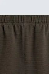 Bermuda de hombre color verde oscuro, de corte relajado y tiro medio. Confeccionada en tejido texturado, presenta cintura elástica con cordón de ajuste interno y bolsillos laterales y trasero de vivo.